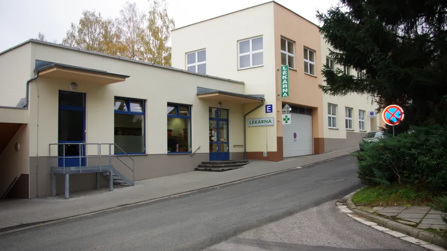 Pohled na světlou budovu lékárny ve svahu, s bezbariérovým přístupem a nápisem „LÉKÁRNA“ u vstupu.
